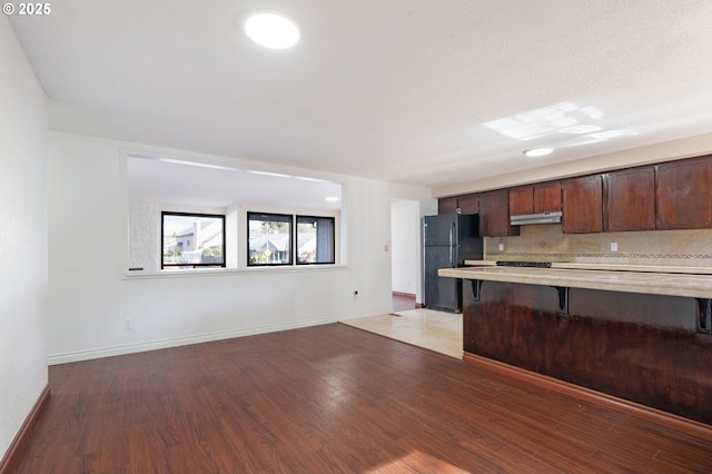 kitchen with light wood finished floors, under cabinet range hood, light countertops, a kitchen breakfast bar, and freestanding refrigerator