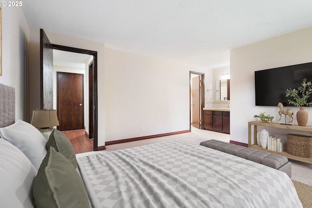 bedroom with connected bathroom, baseboards, and light colored carpet