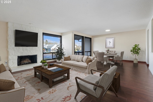 living area with a stone fireplace, wood finished floors, baseboards, and a textured ceiling