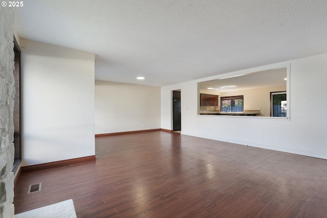 unfurnished living room featuring visible vents, baseboards, a textured ceiling, and wood finished floors