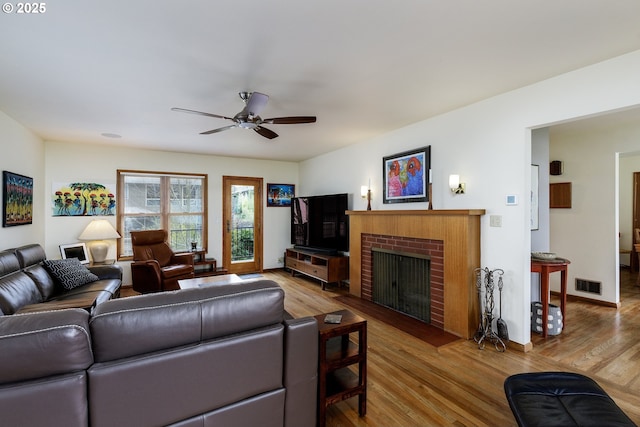 living area with visible vents, a brick fireplace, wood finished floors, and a ceiling fan