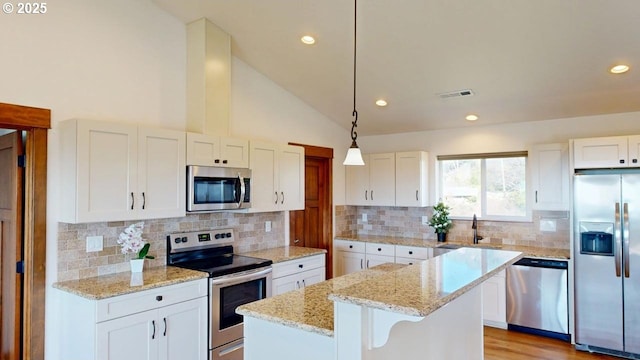 kitchen with a sink, a center island, lofted ceiling, stainless steel appliances, and white cabinets