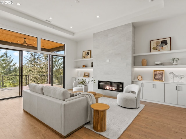 living room with built in shelves, a fireplace, recessed lighting, and light wood-style flooring
