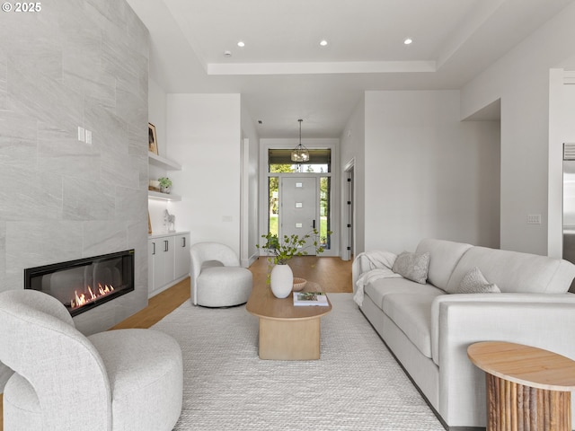living room featuring a fireplace, a raised ceiling, wood finished floors, and recessed lighting