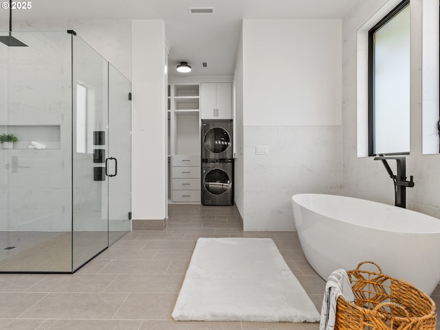 full bathroom featuring tile patterned floors, a stall shower, a freestanding tub, stacked washer and clothes dryer, and visible vents