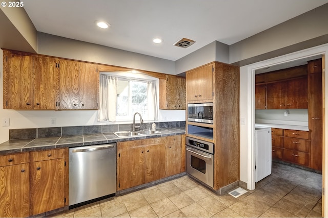 kitchen featuring brown cabinetry, visible vents, stainless steel appliances, and a sink