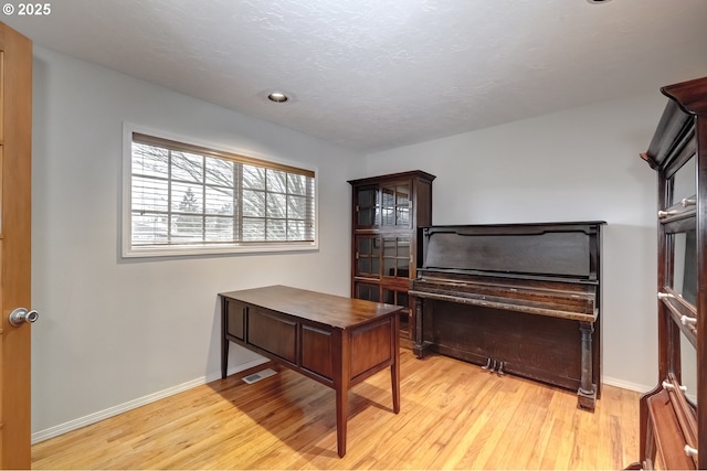 home office featuring a textured ceiling, light wood finished floors, visible vents, and baseboards