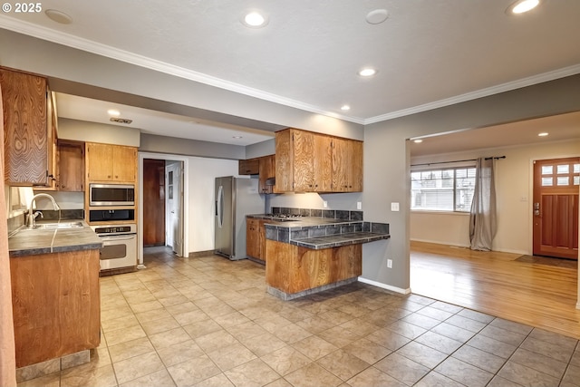 kitchen featuring brown cabinets, appliances with stainless steel finishes, ornamental molding, a sink, and a peninsula