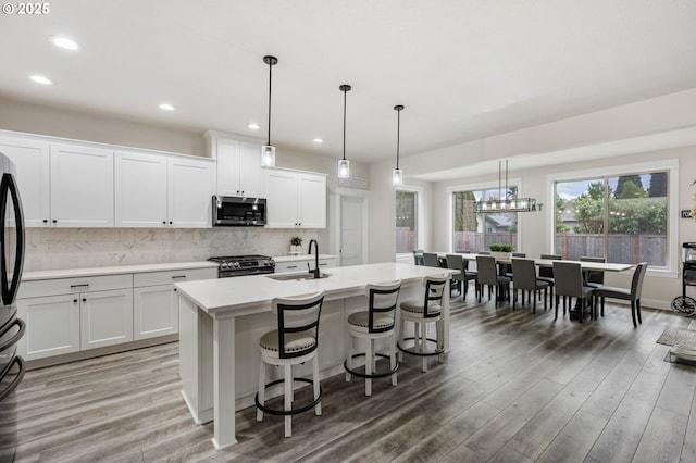 kitchen with appliances with stainless steel finishes, a center island with sink, a sink, light countertops, and light wood-style floors