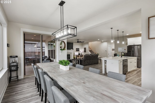 dining area with stairs, a fireplace, ceiling fan, light wood-type flooring, and recessed lighting