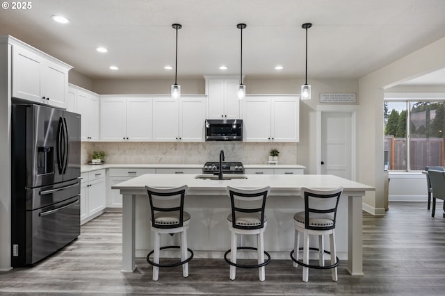 kitchen featuring a kitchen island with sink, a kitchen breakfast bar, light countertops, stainless steel microwave, and refrigerator with ice dispenser