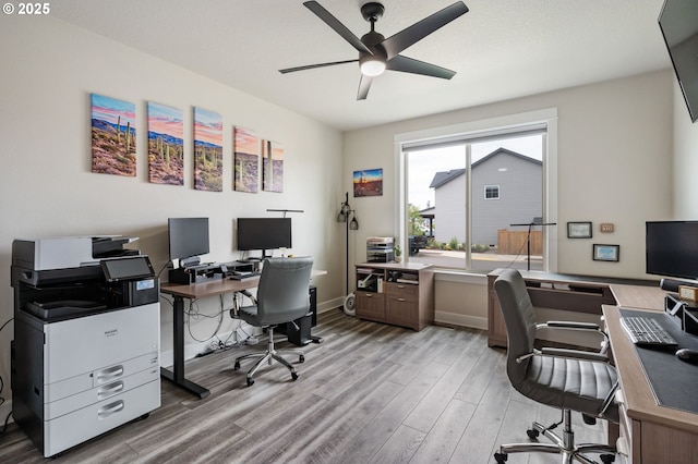 office space featuring a ceiling fan, baseboards, and light wood finished floors