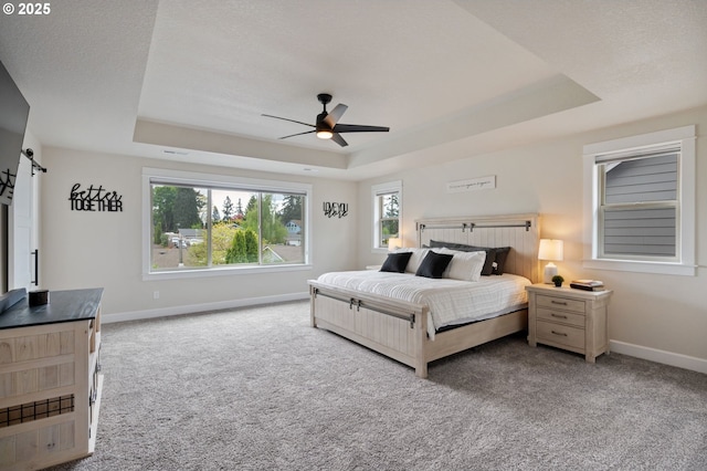 carpeted bedroom featuring a tray ceiling, ceiling fan, a barn door, and baseboards