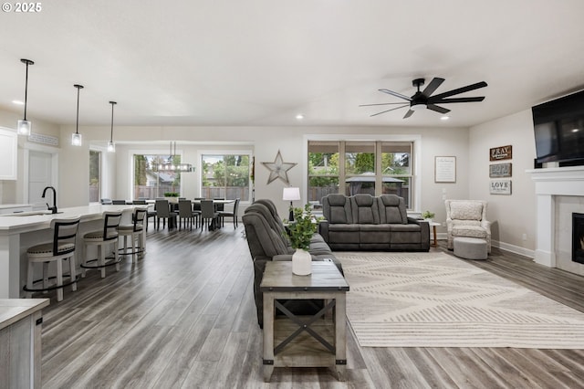 living room featuring a fireplace, ceiling fan with notable chandelier, recessed lighting, and wood finished floors