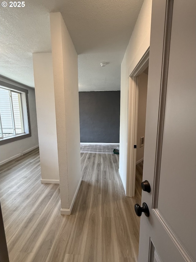 corridor featuring baseboards, a textured ceiling, and wood finished floors