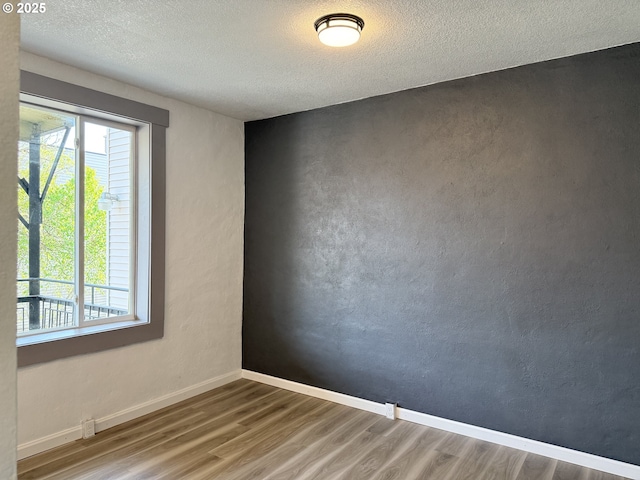 spare room featuring a textured ceiling, baseboards, and wood finished floors