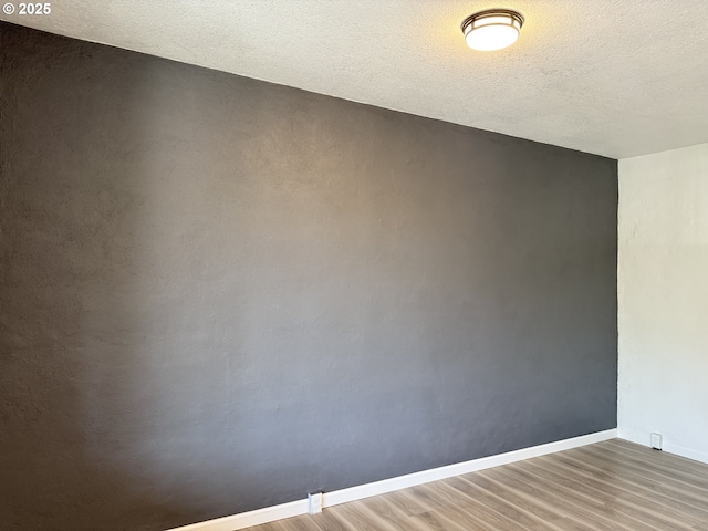 unfurnished room with baseboards, a textured ceiling, and wood finished floors