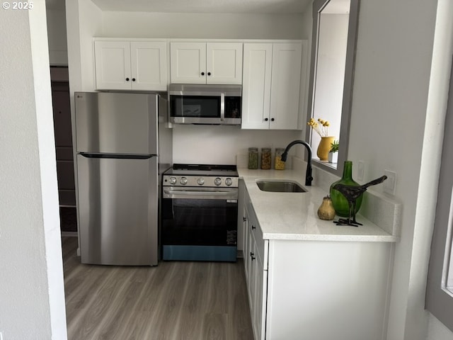 708 N Killingsworth St Unit 7, Portland, OR 97217 - kitchen featuring appliances with stainless steel finishes, a sink, light wood-style floors, light countertops, and white cabinetry