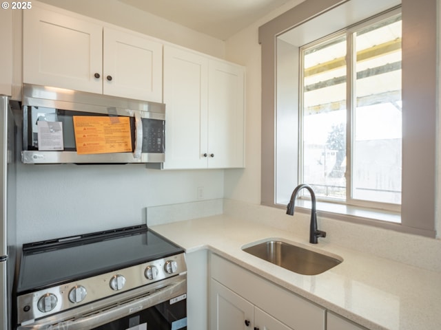 kitchen featuring a sink, white cabinets, light stone counters, and stainless steel appliances