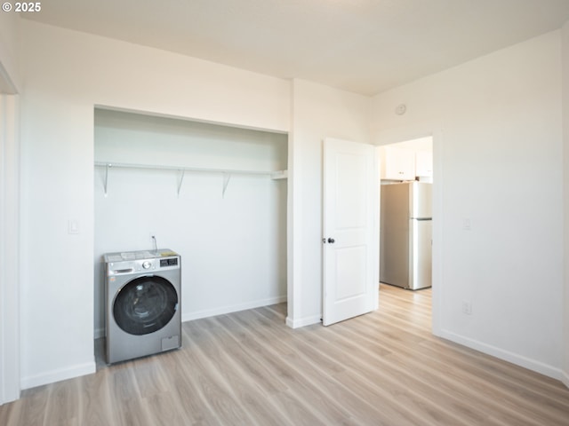 clothes washing area featuring washer / dryer, baseboards, laundry area, and light wood-style flooring