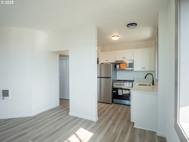 kitchen featuring light wood-style flooring, a sink, white cabinetry, stainless steel appliances, and light countertops