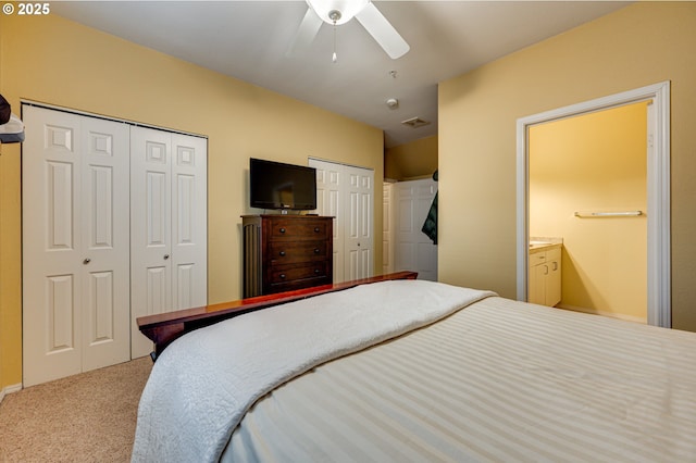 bedroom with two closets, ceiling fan, ensuite bathroom, and carpet flooring