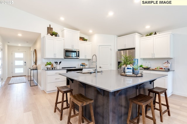 kitchen with a kitchen bar, appliances with stainless steel finishes, a center island with sink, and white cabinetry