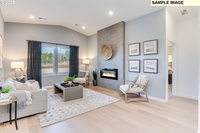 living room with light hardwood / wood-style floors, lofted ceiling, and a tiled fireplace