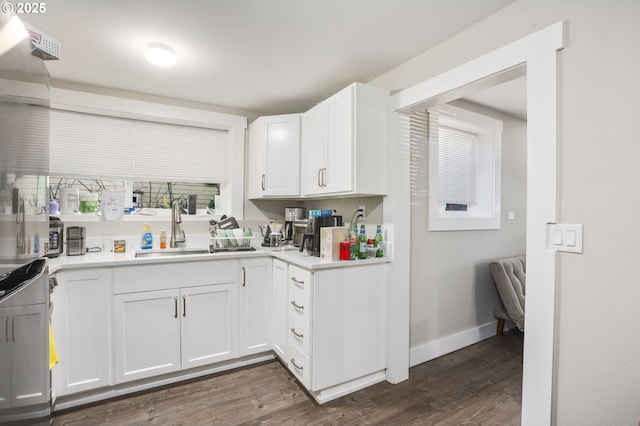 kitchen with a sink, white cabinetry, baseboards, light countertops, and dark wood-style floors