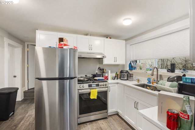 kitchen with light countertops, appliances with stainless steel finishes, white cabinets, a sink, and under cabinet range hood