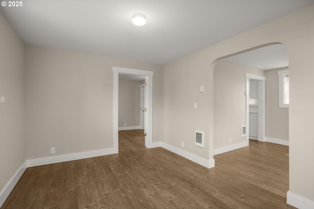 unfurnished room with arched walkways, visible vents, baseboards, and wood finished floors