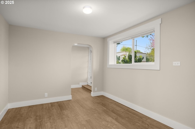 unfurnished room featuring arched walkways, baseboards, and wood finished floors