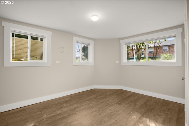 empty room featuring wood finished floors, a wealth of natural light, and baseboards