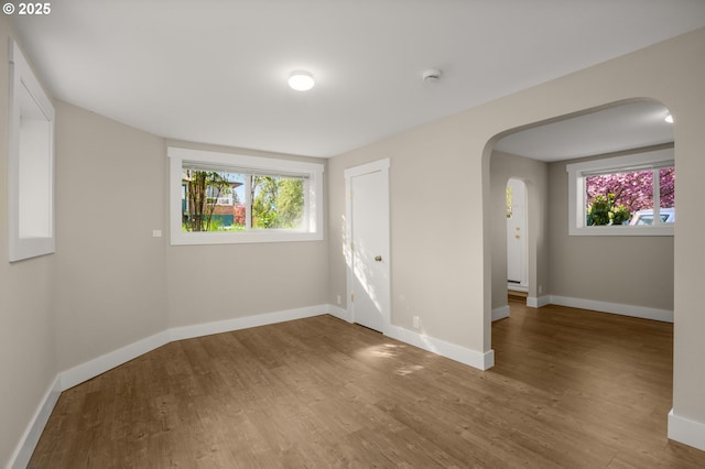 empty room with arched walkways, wood finished floors, a wealth of natural light, and baseboards