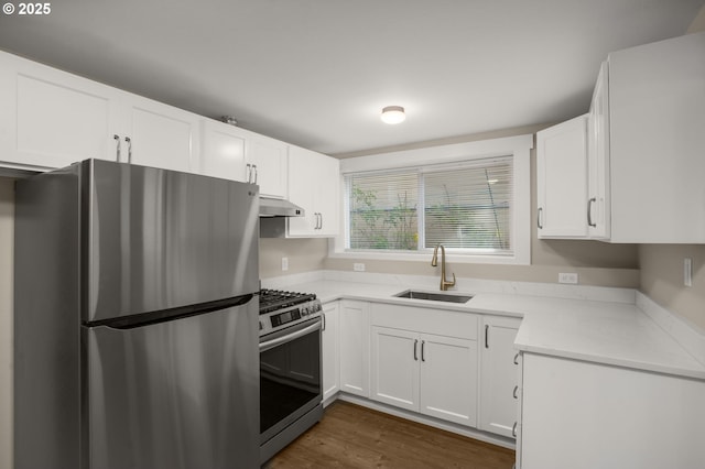 kitchen with dark wood finished floors, stainless steel appliances, white cabinets, a sink, and under cabinet range hood