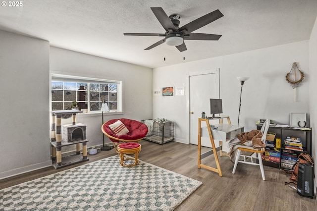 recreation room with ceiling fan, a textured ceiling, baseboards, and wood finished floors