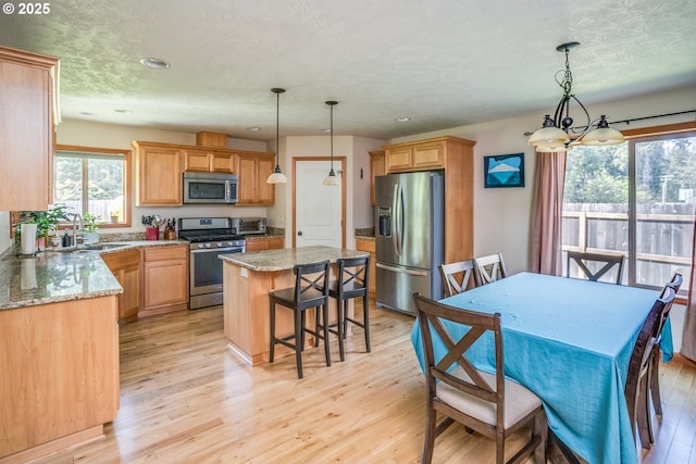 kitchen featuring stainless steel appliances, a sink, a center island, light wood-style flooring, and a chandelier