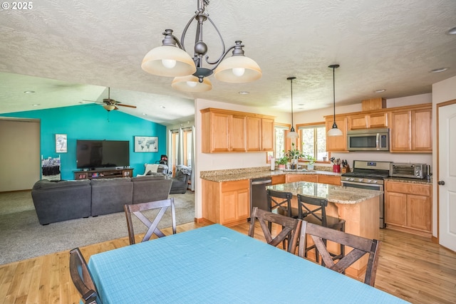 kitchen with stainless steel appliances, light wood finished floors, a ceiling fan, a textured ceiling, and decorative light fixtures
