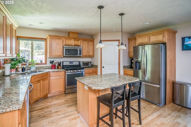 kitchen featuring stainless steel appliances, a sink, a kitchen island, light wood-style floors, and light stone counters