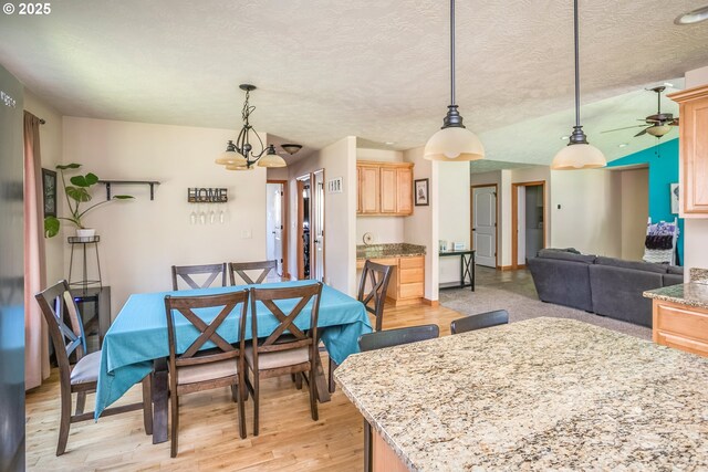 dining space with light wood-style flooring, a ceiling fan, a textured ceiling, and a chandelier