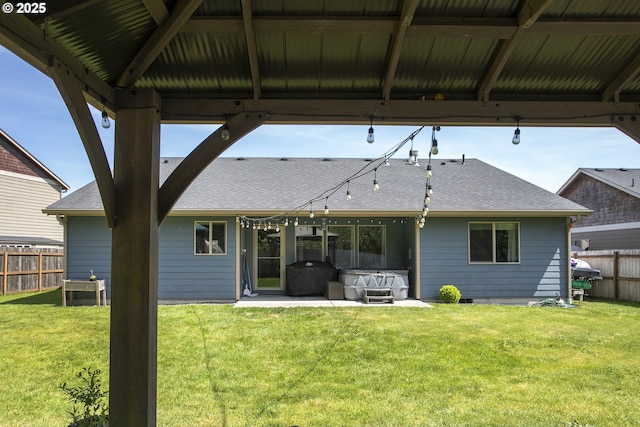 back of property featuring roof with shingles, a patio area, and a hot tub