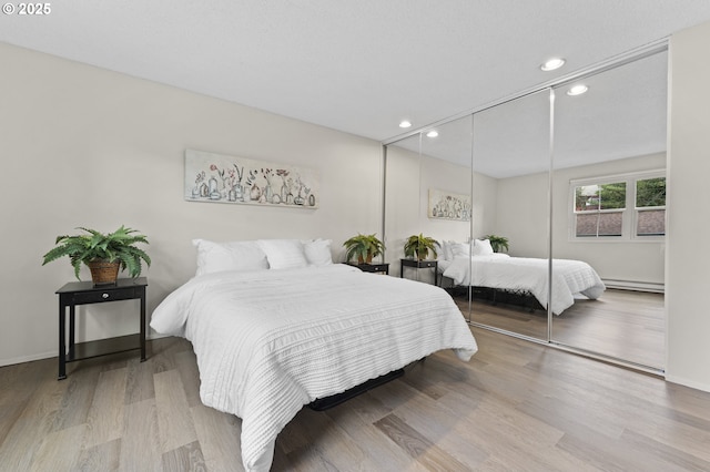 bedroom featuring a closet, light wood-type flooring, and a baseboard heating unit