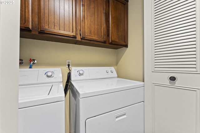 clothes washing area with washing machine and clothes dryer and cabinets