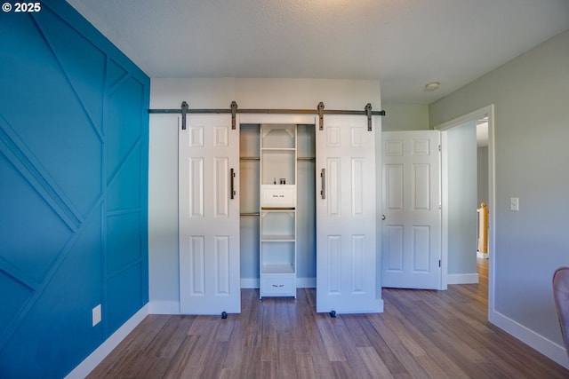 unfurnished bedroom with hardwood / wood-style flooring, a barn door, and a closet