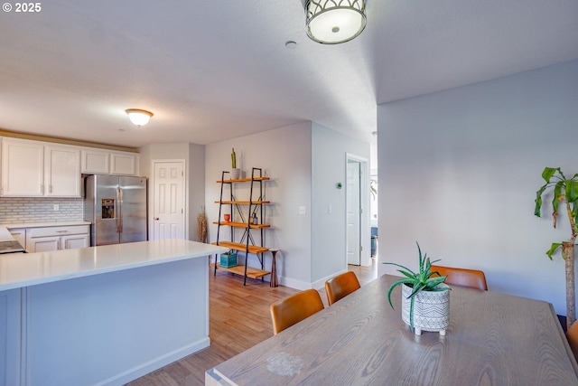 kitchen with a breakfast bar area, white cabinets, decorative backsplash, stainless steel fridge with ice dispenser, and light wood-type flooring