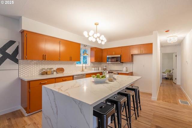 kitchen with a kitchen island, an inviting chandelier, appliances with stainless steel finishes, and light hardwood / wood-style floors