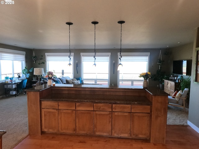 kitchen featuring brown cabinets, dark stone counters, open floor plan, and decorative light fixtures