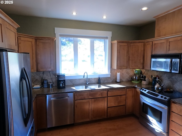 kitchen with tasteful backsplash, brown cabinetry, dark stone counters, appliances with stainless steel finishes, and a sink