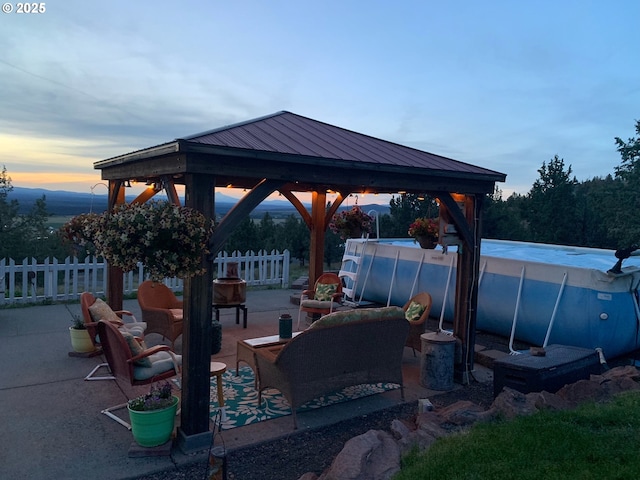 patio terrace at dusk with fence, a hot tub, and a gazebo