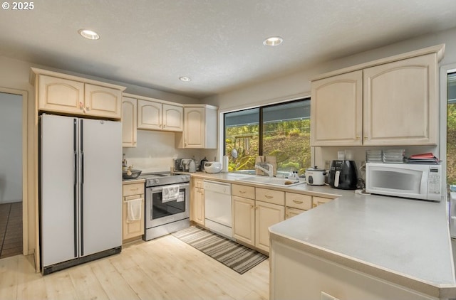 kitchen featuring white appliances, light brown cabinets, a sink, recessed lighting, and light countertops